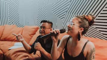 A room with a geometric patterned wall, a bed with orange bedding, and a person holding a microphone.
