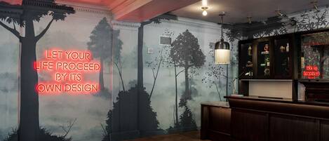 Une pièce dotée d’un plancher en bois, d’un coin bar avec des étagères et d’un mur orné d’une fresque représentant une forêt et d’un panneau néon.