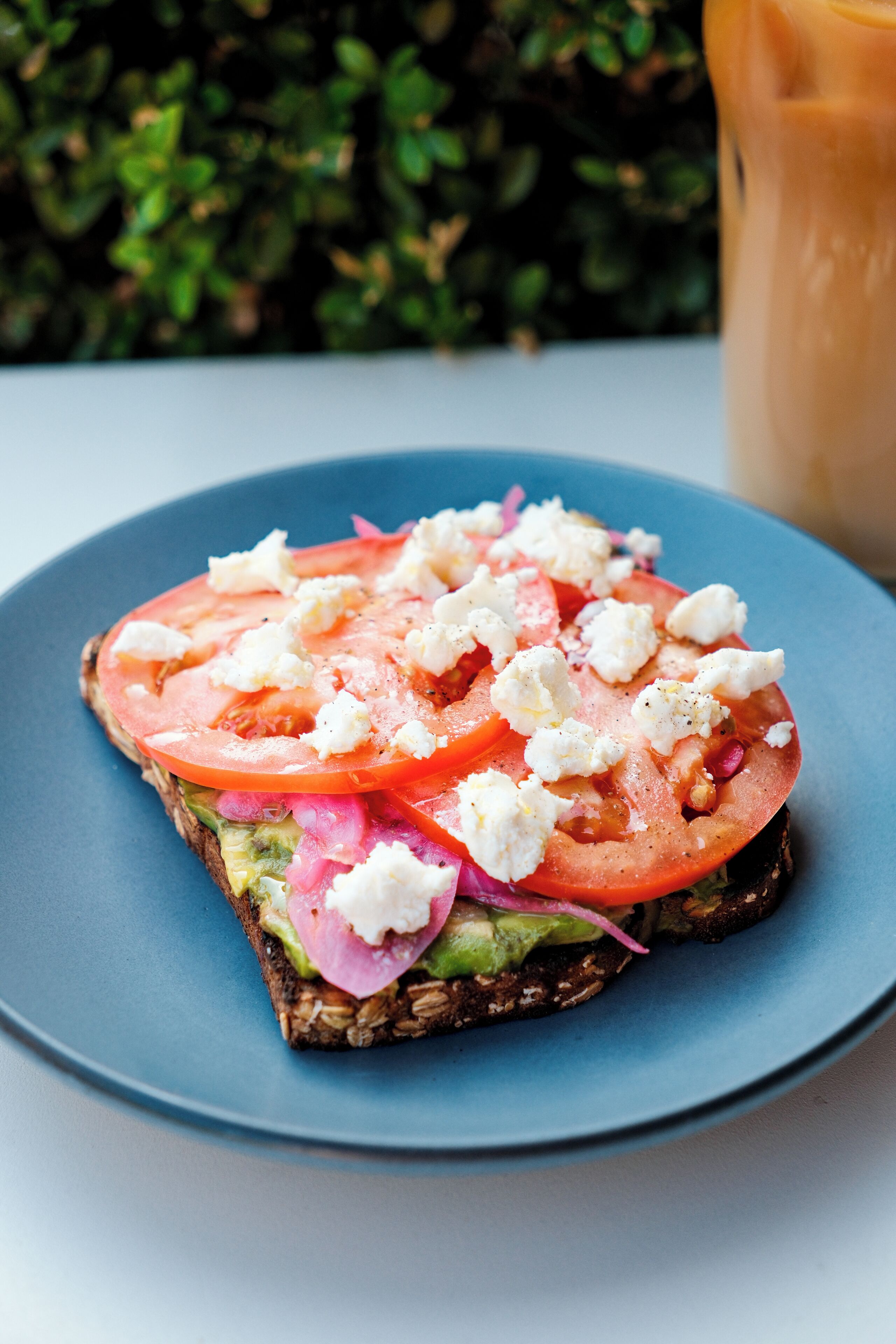 A slice of toast with tomato, onion, and feta cheese on a blue plate.