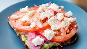 A slice of toast with tomato, onion, and feta cheese on a blue plate.
