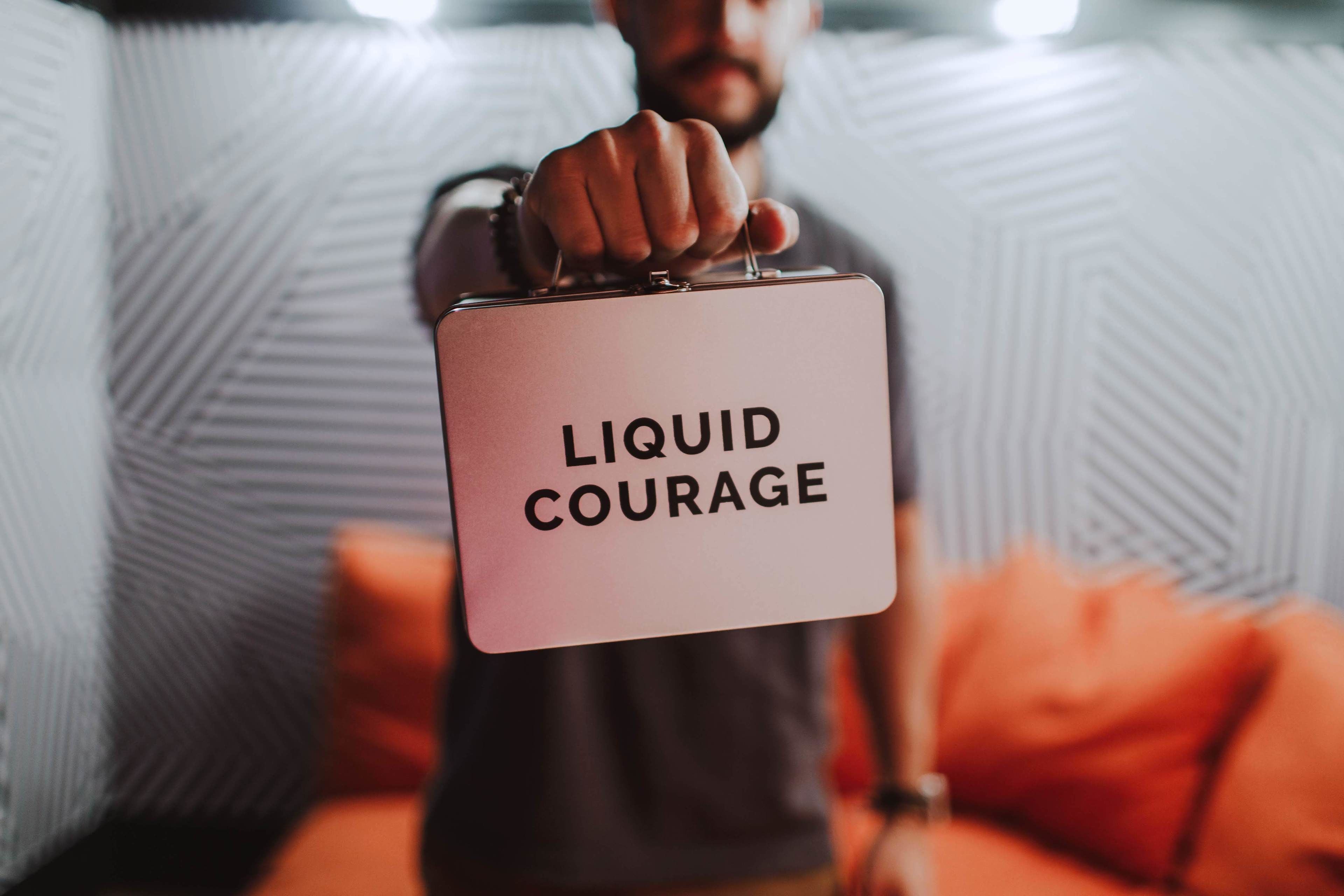 Une personne tenant une valise sur laquelle on peut lire les mots « COURAGE LIQUIDE ».