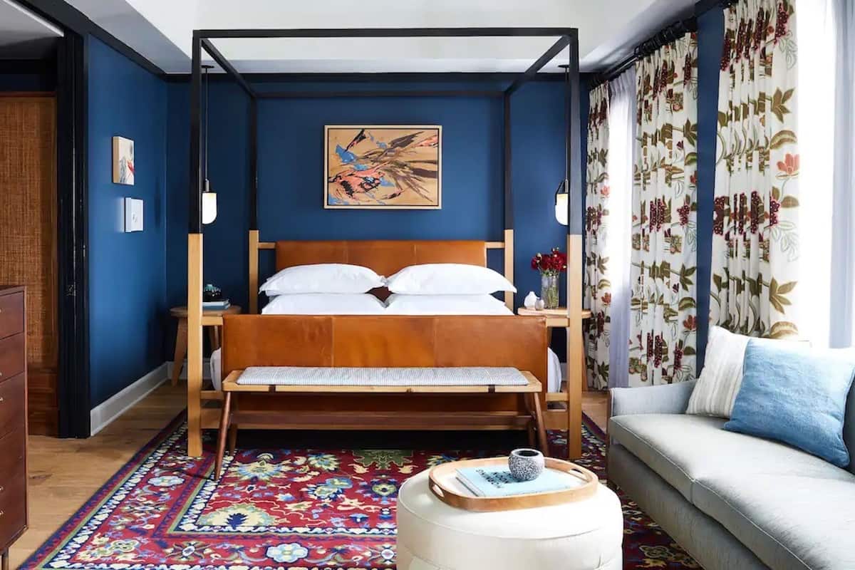 A bedroom with a four-poster bed, a wooden dresser, a sofa, a patterned rug, and a painting on the wall.