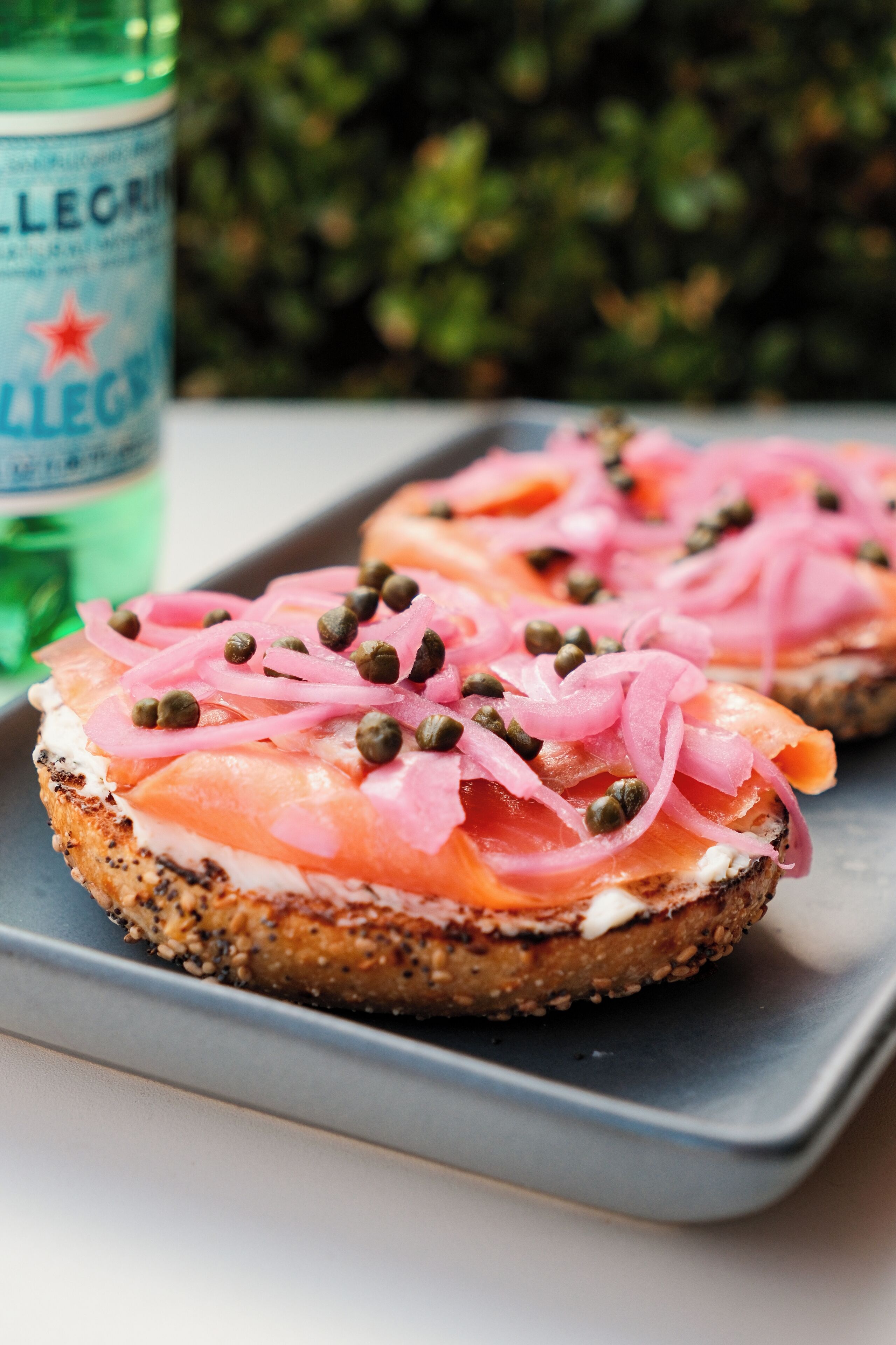 A tray with three open-faced sandwiches topped with smoked salmon, capers, and pickled onions.
