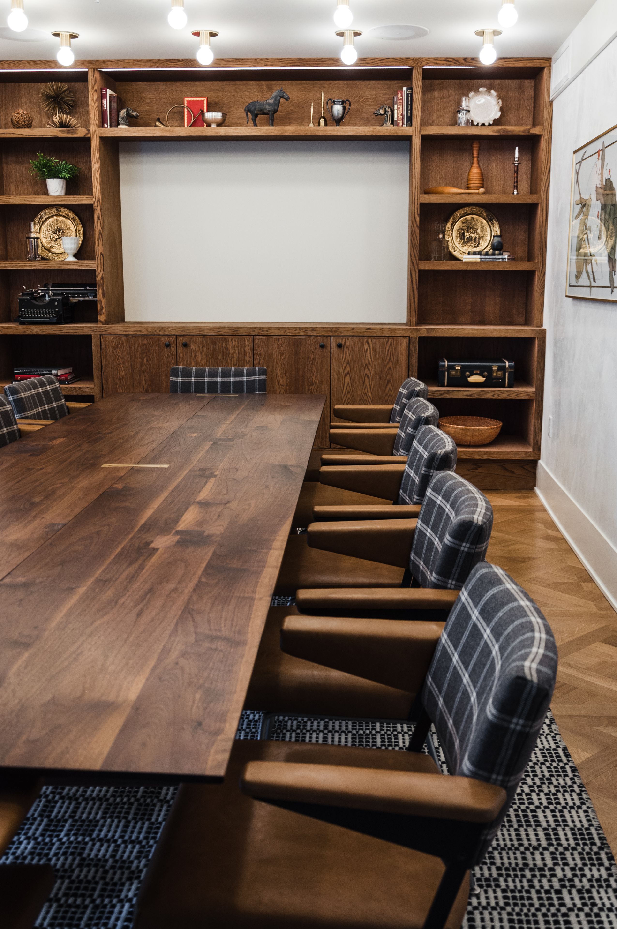 A conference room with a long wooden table, six upholstered chairs, and wooden shelving with various decorative items.