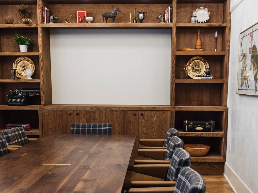 A conference room with a long wooden table, six upholstered chairs, and wooden shelving with various decorative items.