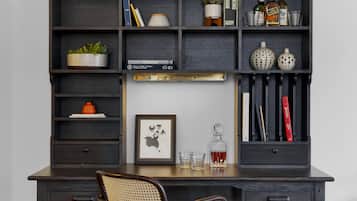 Een donker houten bureau met planken waarop boeken, een potplant, een ingelijst beeld en een glas whisky staan.