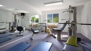 A gym with exercise equipment, mats, and a large window with a view of trees.