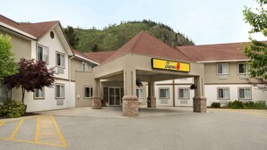 A Super 8 hotel with a parking lot, beige exterior, and a mountain backdrop.
