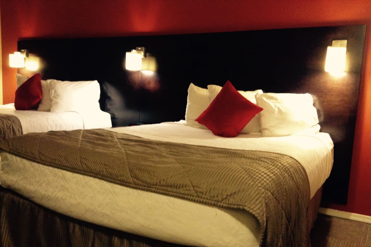 Ett hotellrum med två sängar, båda med vita sängkläder och röda kuddar, och en mörk sänggavel.