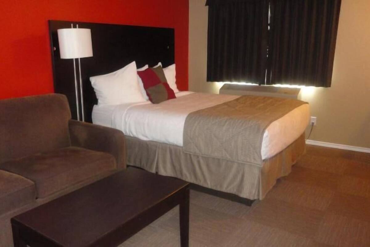 Ein Hotelzimmer mit einem Bett, einem Sofa, einem Nachttisch, einer Lampe und einem Fenster mit Vorhängen.