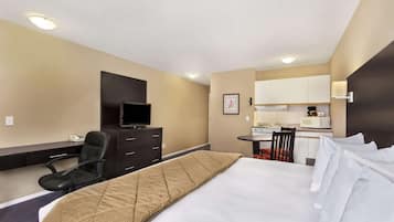 Une chambre d’hôtel comprenant un lit, un bureau, une chaise, une télévision, un coin cuisine et une petite table à manger.