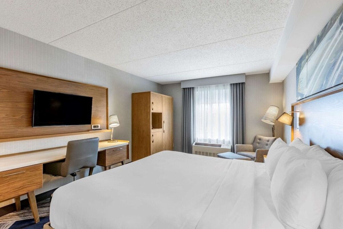 A hotel room with a large bed, a desk with a chair, a television, and a wardrobe.