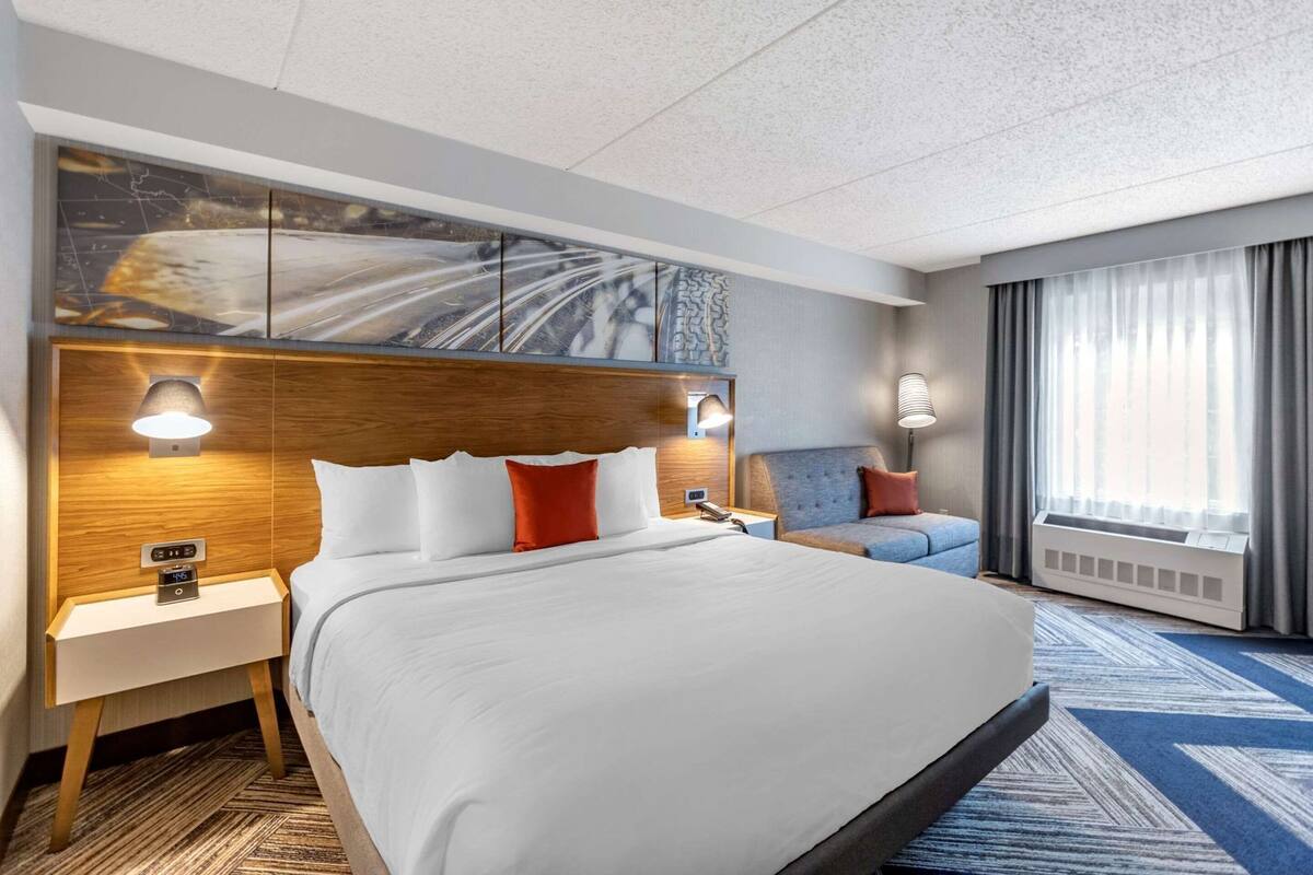 A hotel room with a large bed, bedside tables, a nightstand, a sofa, a wall-mounted artwork, and a window with curtains.