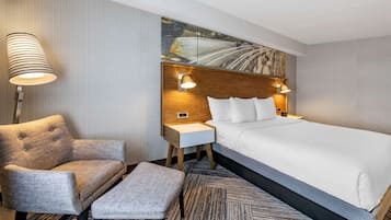 Una habitación de hotel con una cama grande, una silla, una mesita y una lámpara.