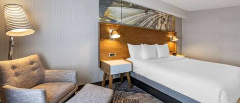 A hotel room with a large bed, a chair, a small table, and a lamp.