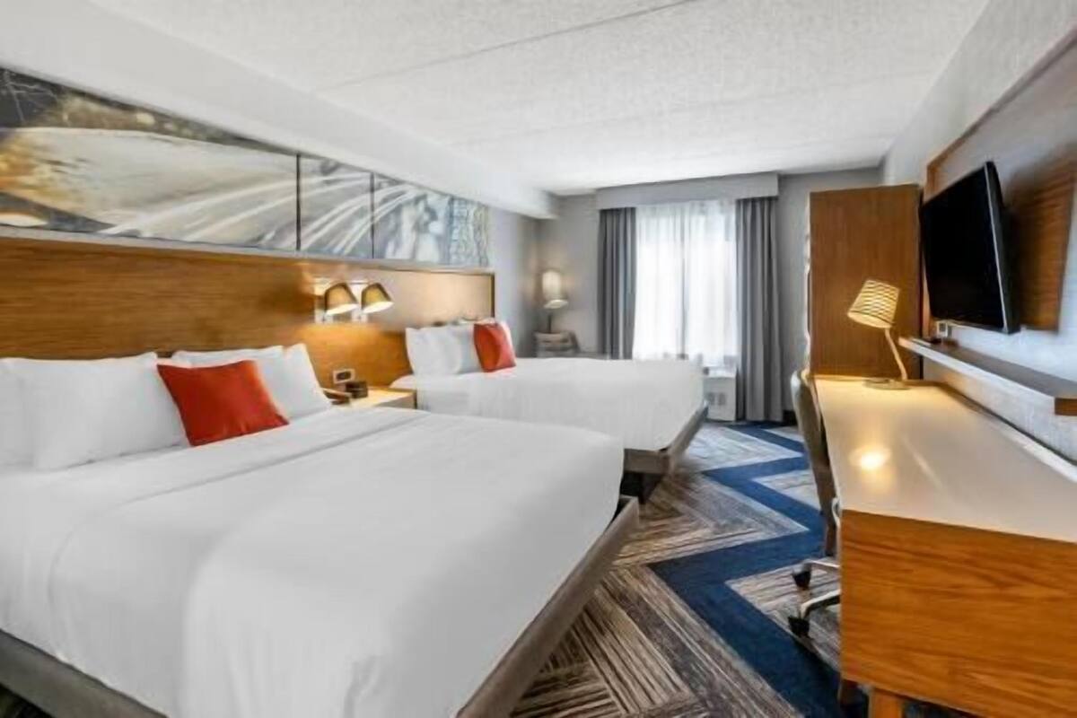 A hotel room with two beds, a desk, a TV, and a window with curtains.