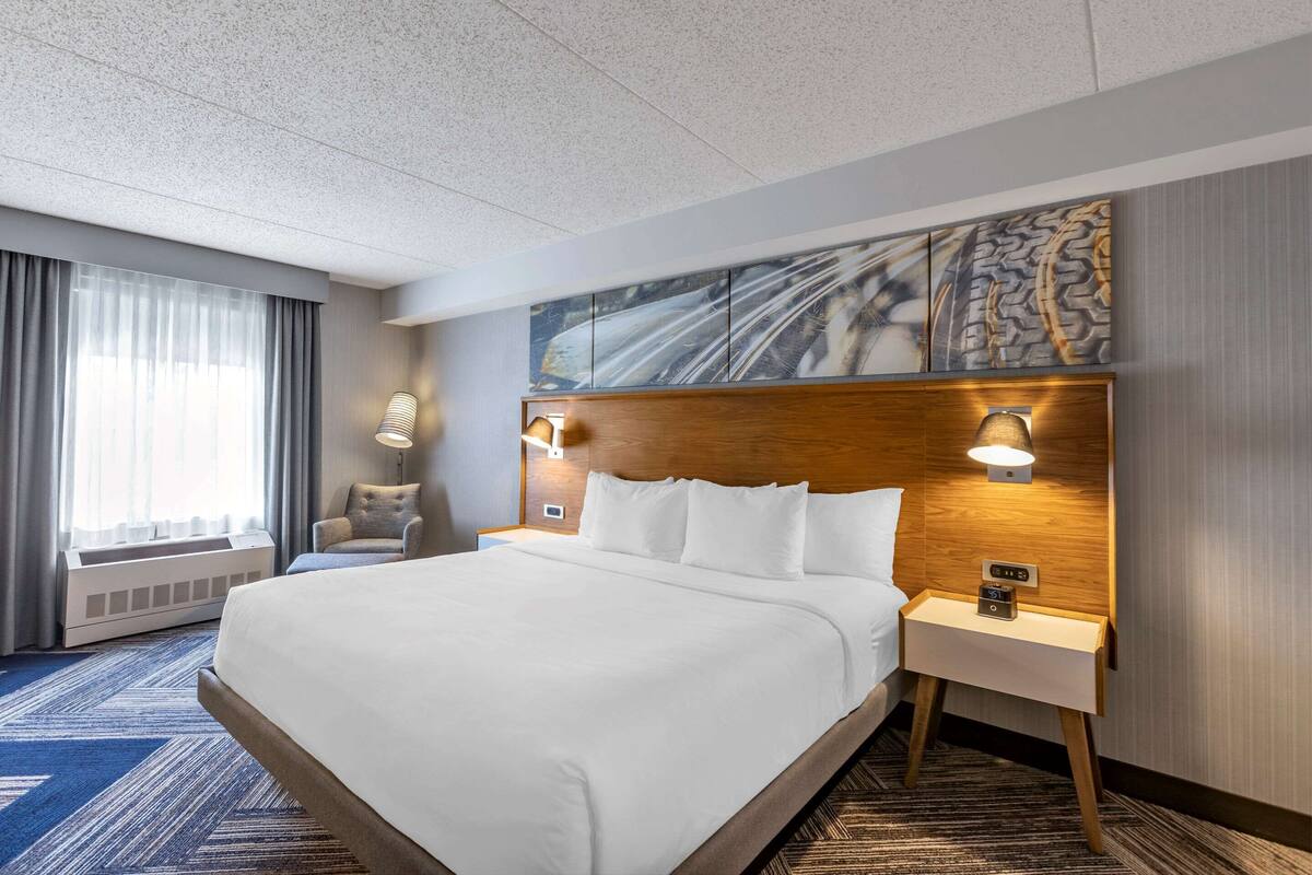 A hotel room with a large bed, two bedside tables with lamps, a wall-mounted artwork, and a window with curtains.