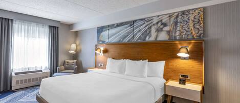 A hotel room with a large bed, two bedside tables with lamps, a wall-mounted artwork, and a window with curtains.