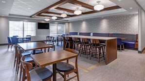 A modern dining area with wooden tables and chairs, a long communal table, and a seating area with a patterned wall. - Comfort Inn Sarnia (Sarnia)