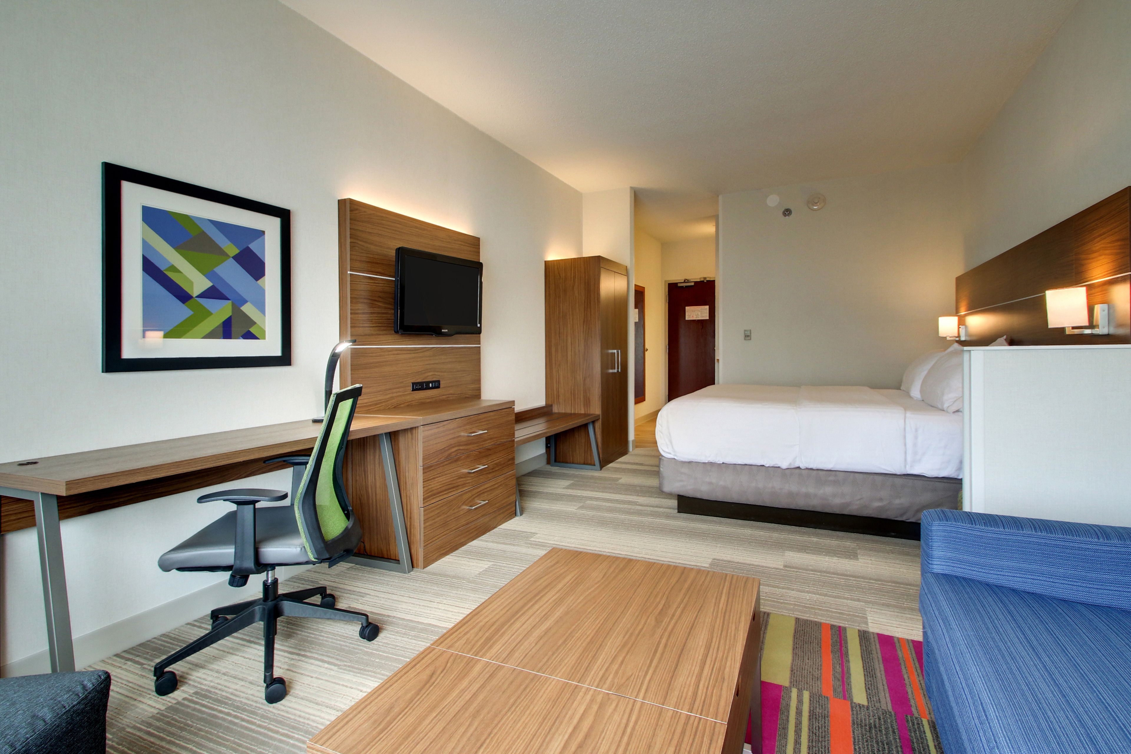 Ein Hotelzimmer mit Bett, Schreibtisch, Stuhl, Fernseher, Kleiderschrank und einem farbenfrohen Teppich.