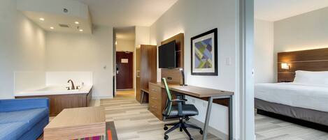 A hotel room with a bed, a desk with a chair, a television, a bathroom with a sink, and a colorful rug.