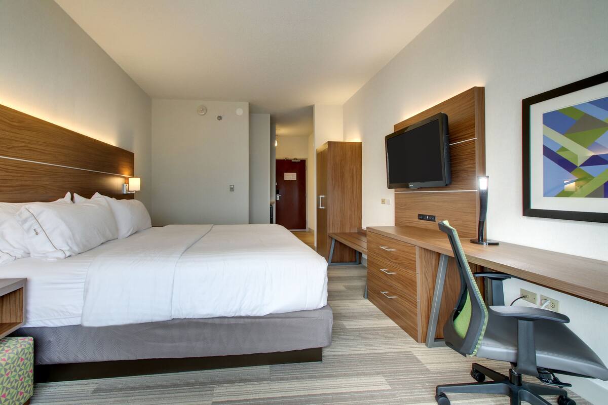 A hotel room with a large bed, a desk with a chair, a flat-screen TV, and a wooden headboard.