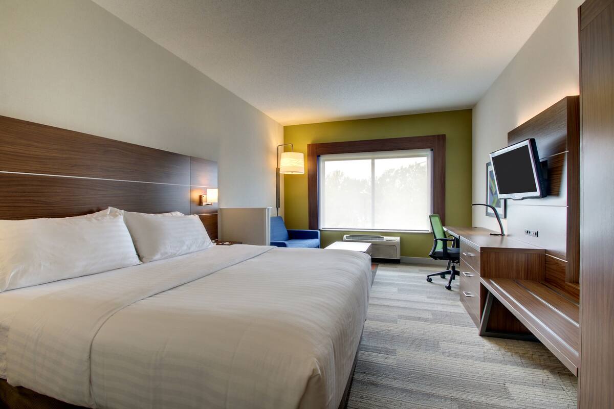 A hotel room with a large bed, a desk, a chair, a TV, and a window.