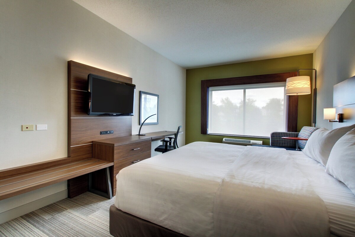 A hotel room with a bed, a desk, a television, a window, and a chair.