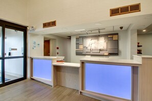 A reception area with a modern design, featuring a glass door entrance, a reception desk with a digital display, and a wall-mounted sign indicating holiday rates. - Holiday Inn Express & Suites Aurora - Naperville by IHG (Aurora)