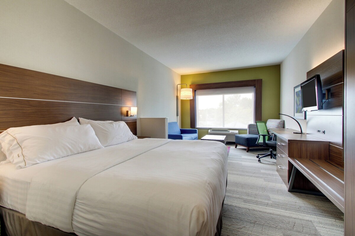 A hotel room with a large bed, a desk with a computer, a chair, and a television.