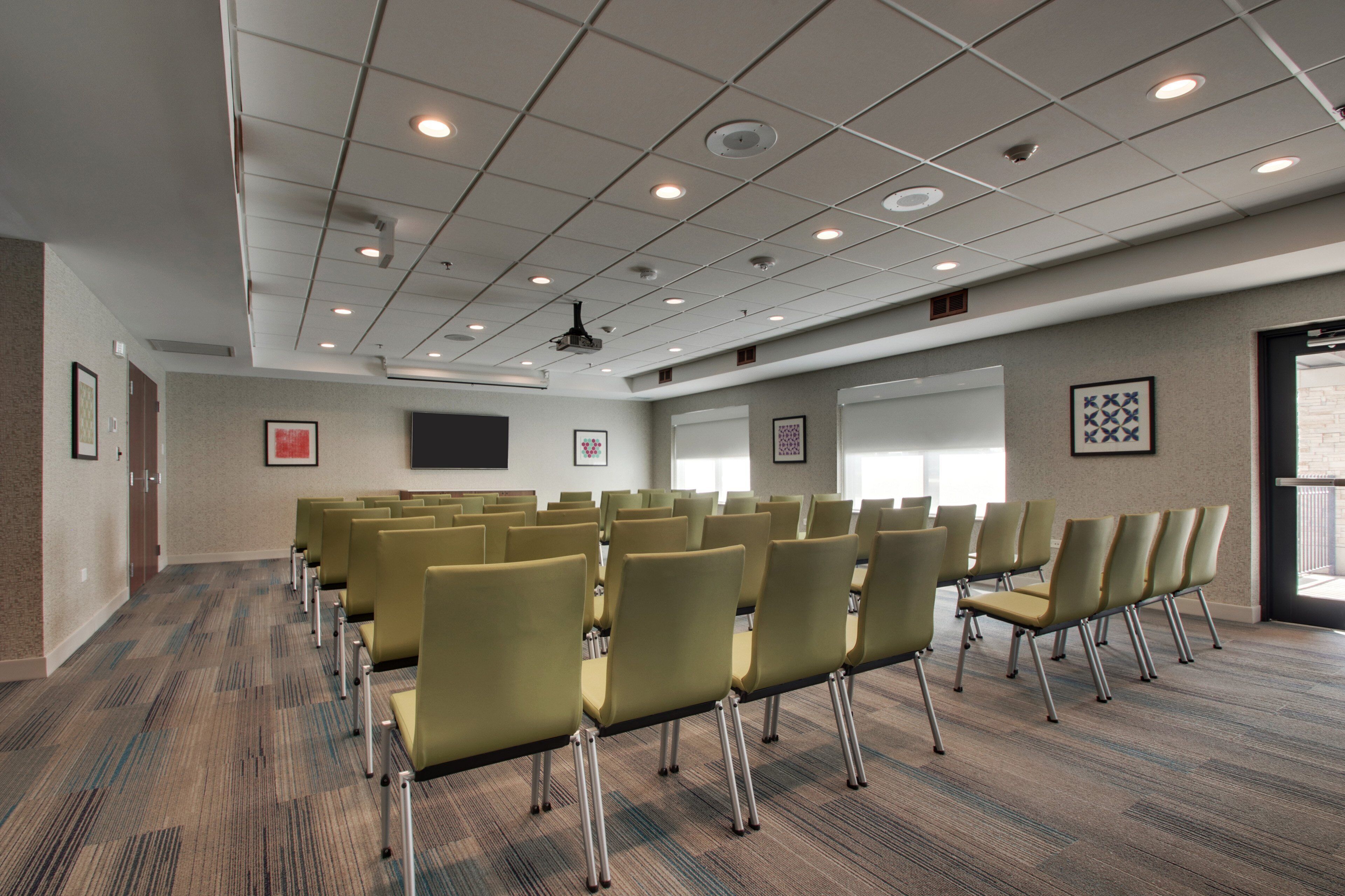 A conference room with rows of chairs, a projector screen, and framed artwork on the walls.
