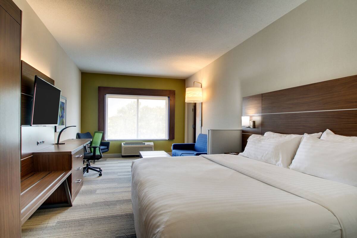 A hotel room with a large bed, a desk with a chair, a television, and a window with natural light.