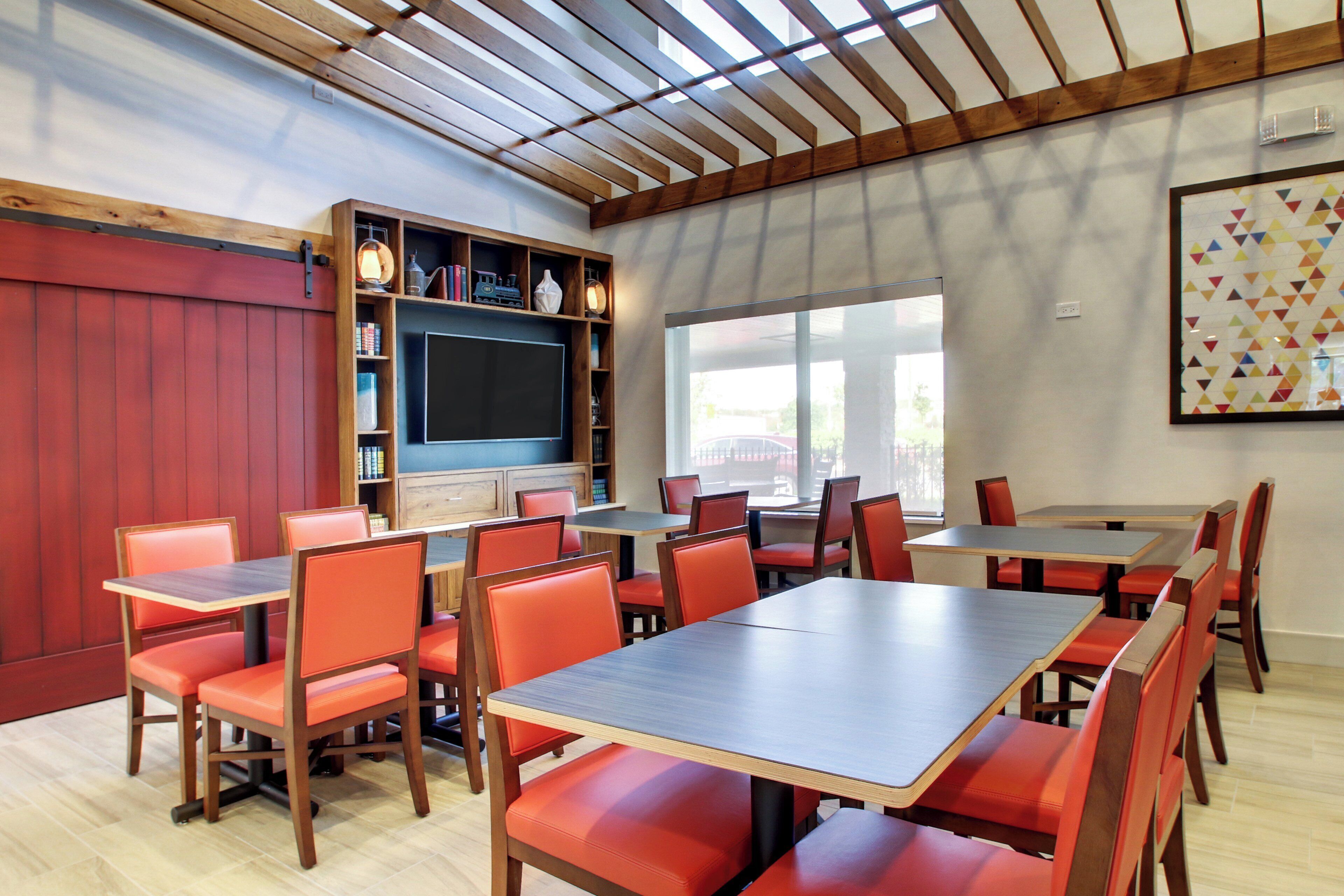 A restaurant with wooden tables and red chairs, a television, and a bookshelf with various items.