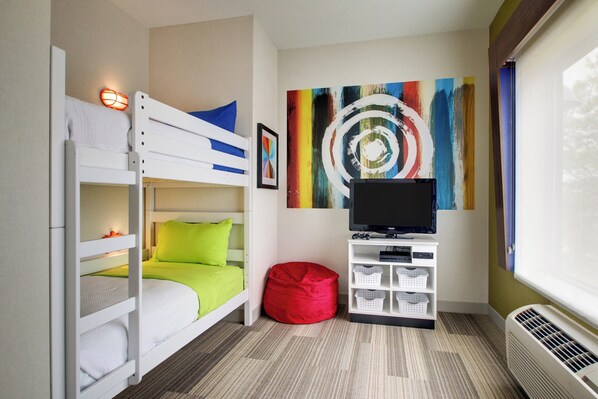 Habitación compacta con literas, un televisor de pantalla plana, un cuadro abstracto colorido y un pequeño sillón de peluche rojo.
