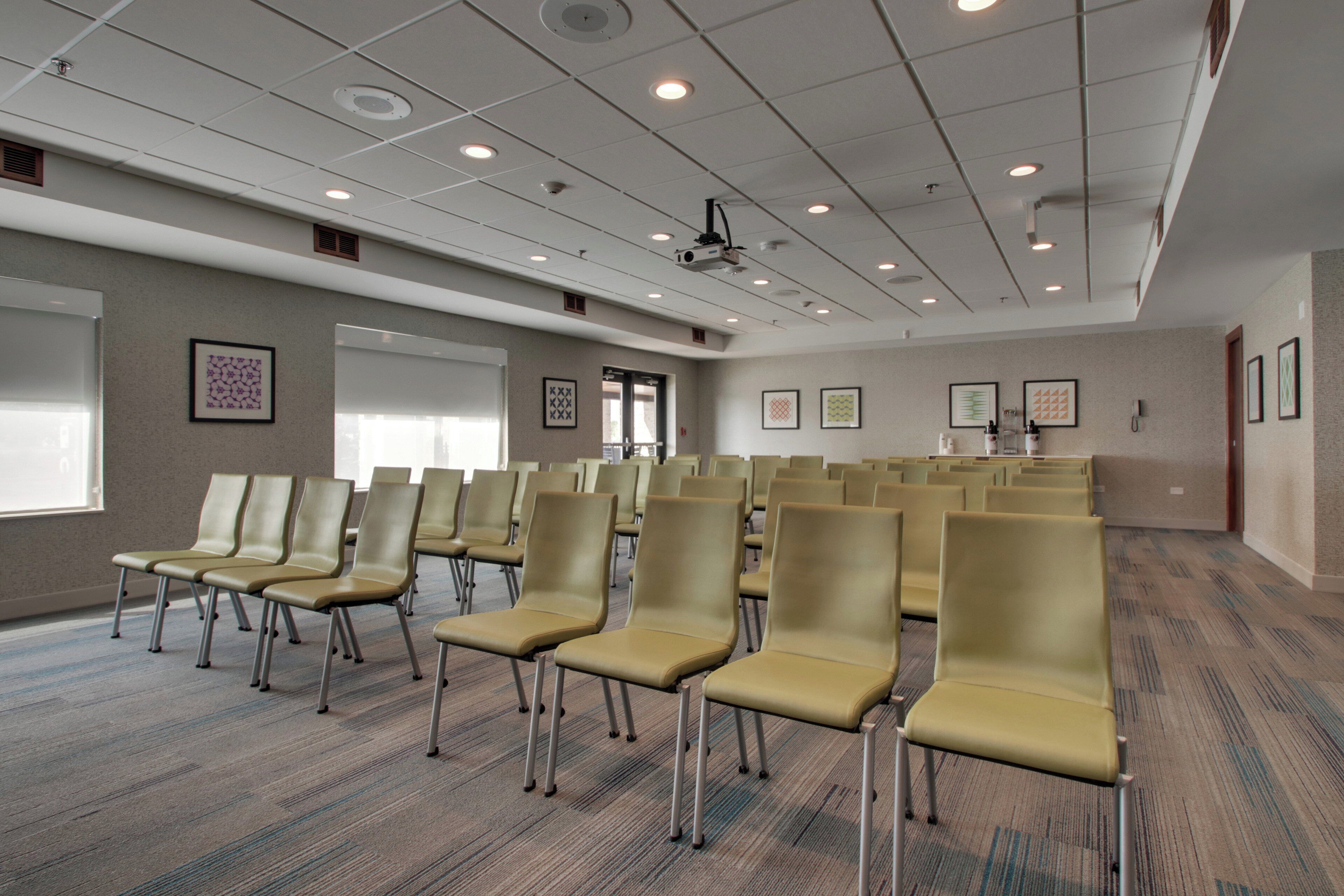 A conference room with rows of chairs, a projector screen, and framed artwork on the walls.