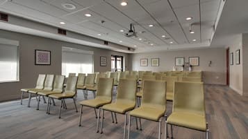 A conference room with rows of chairs, a projector screen, and framed artwork on the walls.