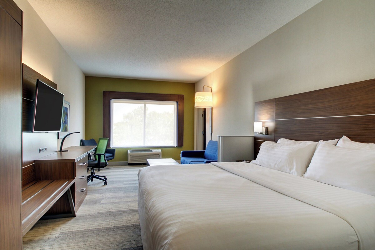 A hotel room with a bed, desk, chair, TV, and a window.