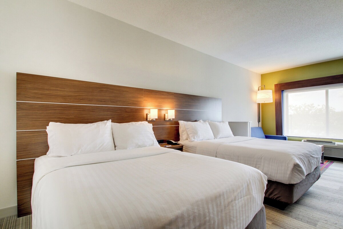 A hotel room with two beds, a wooden headboard, bedside lamps, and a large window.
