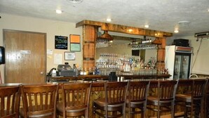 Una zona de bar con taburetes de madera, una barra con botellas y un refrigerador.