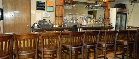 Un espace bar avec des tabourets de bar en bois, un comptoir de bar orné de bouteilles et un réfrigérateur.