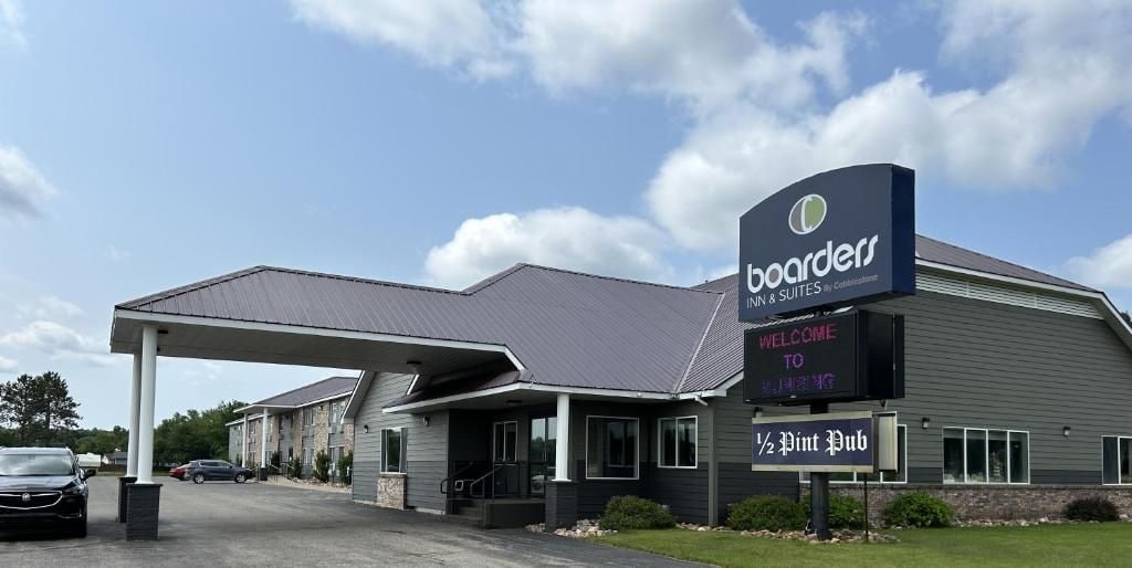 Un edificio con un letrero que dice 'boarders INN & QUITES by Colbystone' y un cartel de bienvenida. Hay un área de estacionamiento techada y un letrero que anuncia '1/2 Pint Pub'.