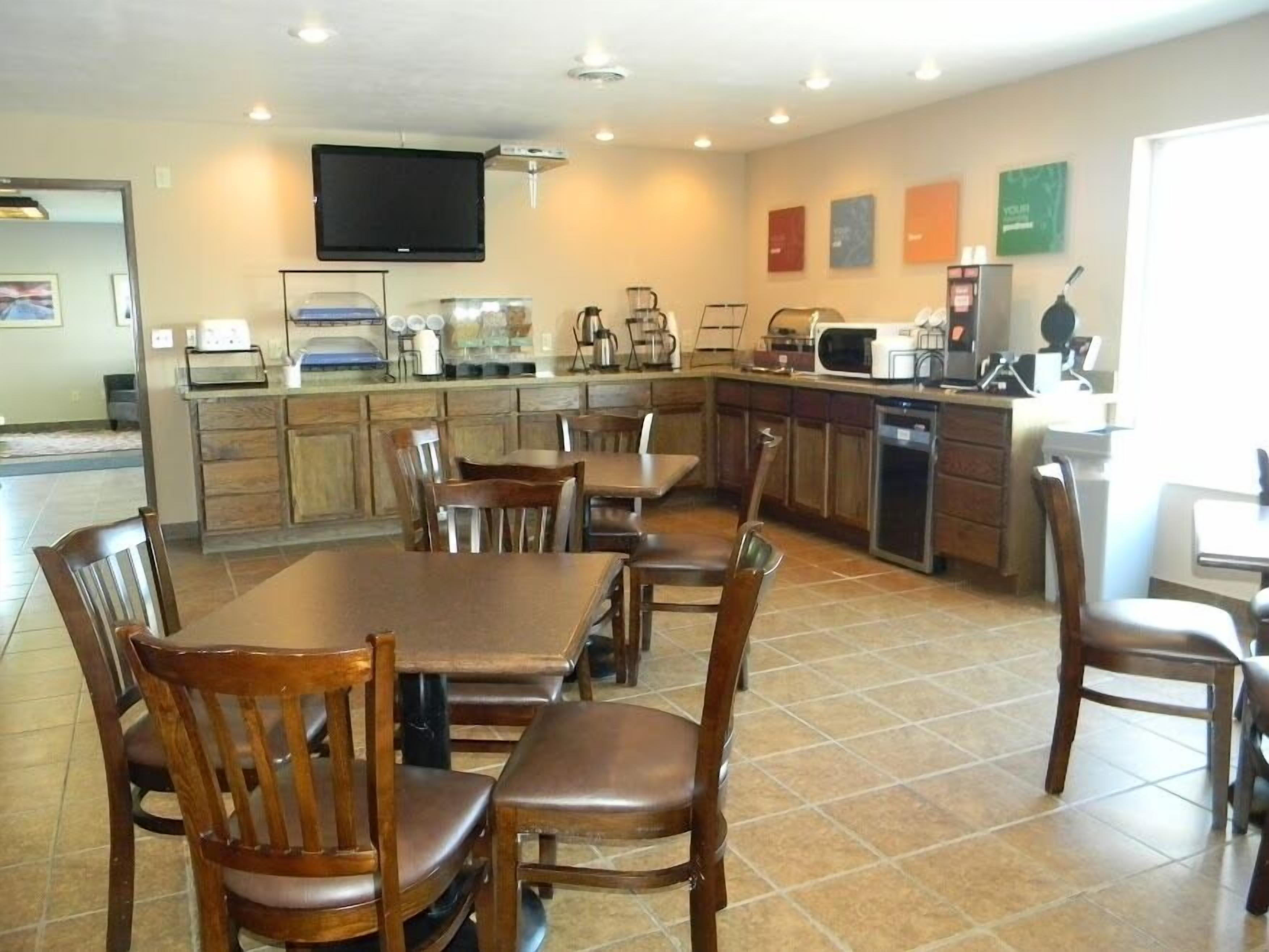 A modern kitchen with wooden cabinets, a dining area with a large table and chairs, and a flat-screen TV mounted above the counter.