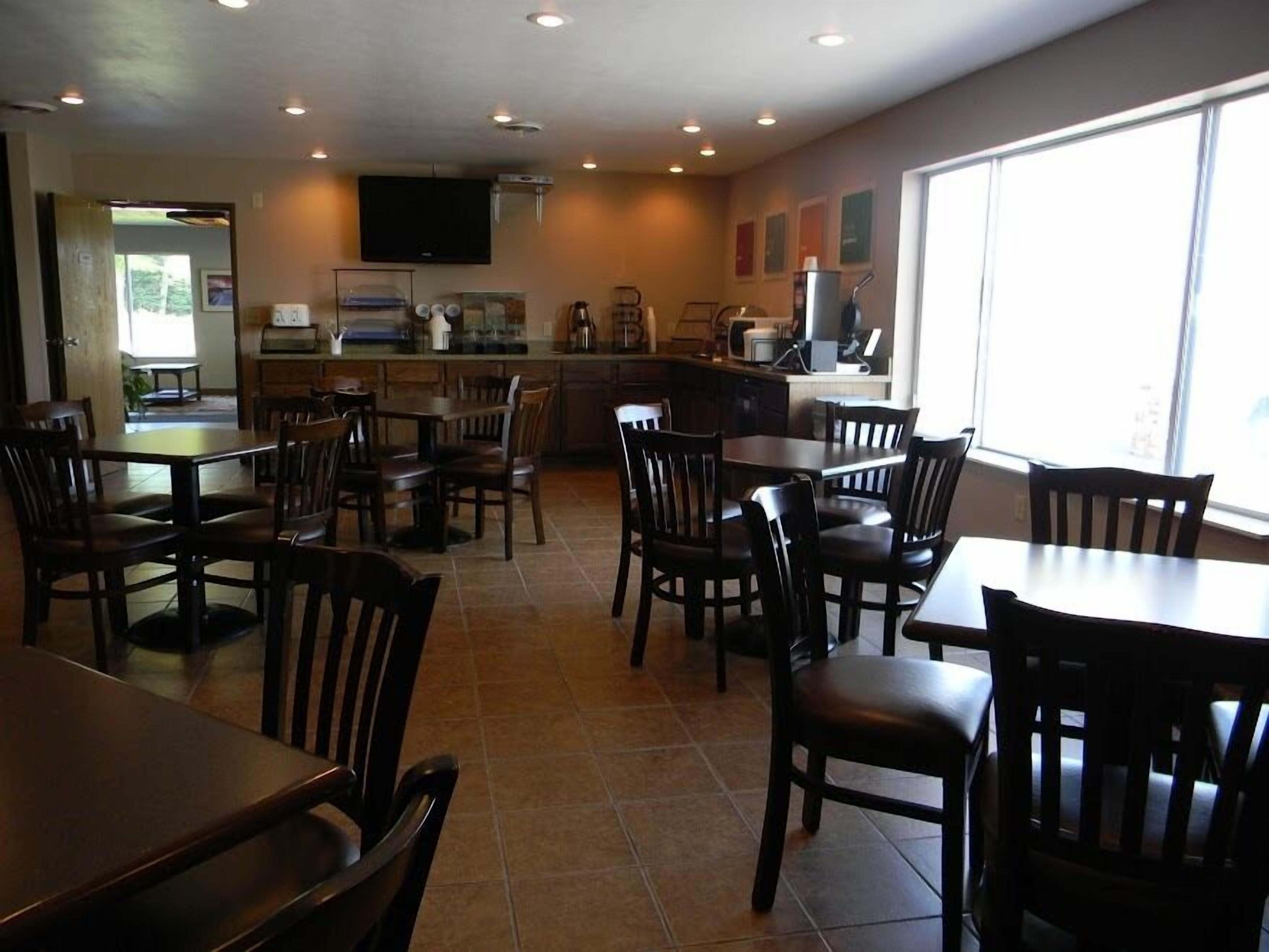 A restaurant with multiple tables and chairs, a kitchen area, and a large window providing natural light.