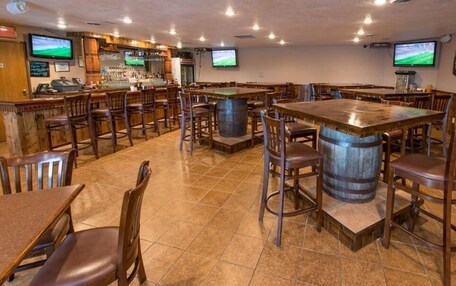 A bar area with wooden tables and chairs, a bar counter, and two televisions mounted on the wall.