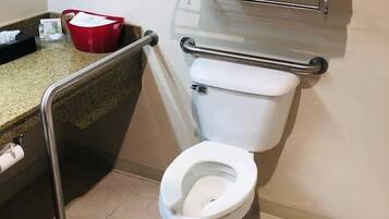 A bathroom with a toilet, a handrail, a red basket, and a towel rack.