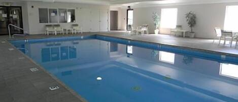 An indoor swimming pool with clear water, surrounded by a tiled floor and white walls.