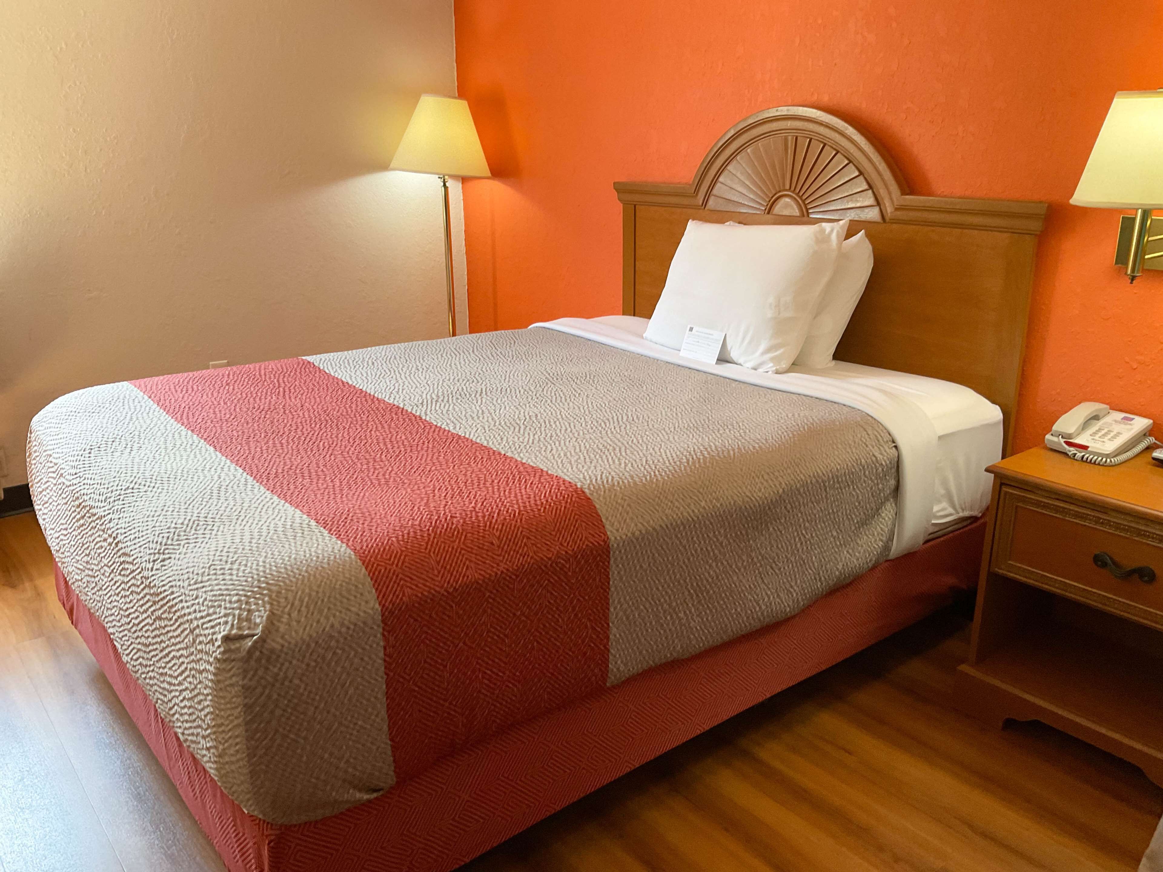 Habitación de hotel con una cama, dos lámparas de noche, una mesita de noche con un teléfono y una pared naranja.