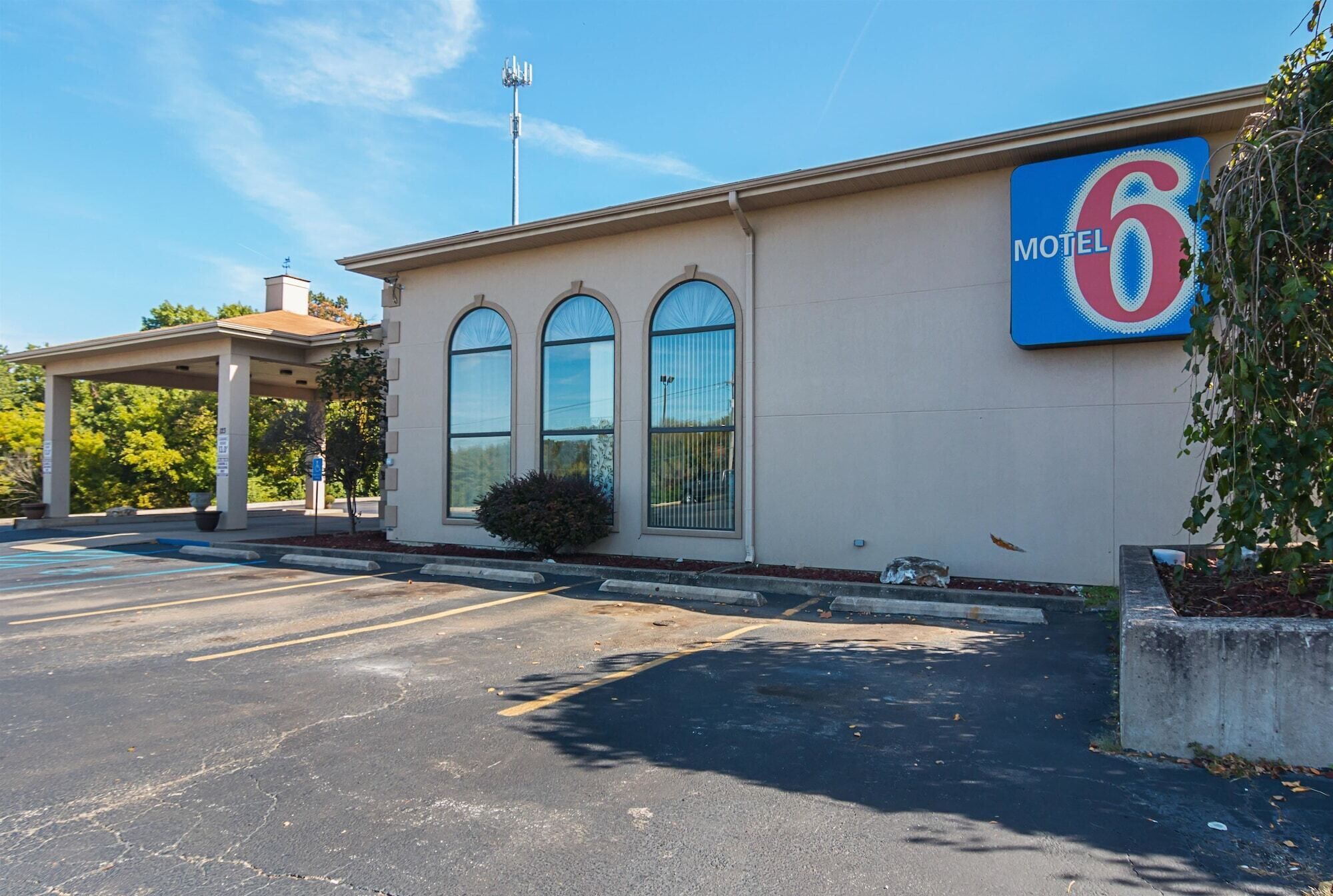 Un motel avec un grand panneau indiquant le chiffre « 6 », un espace de stationnement couvert et un bâtiment doté de trois fenêtres en arc de cercle.