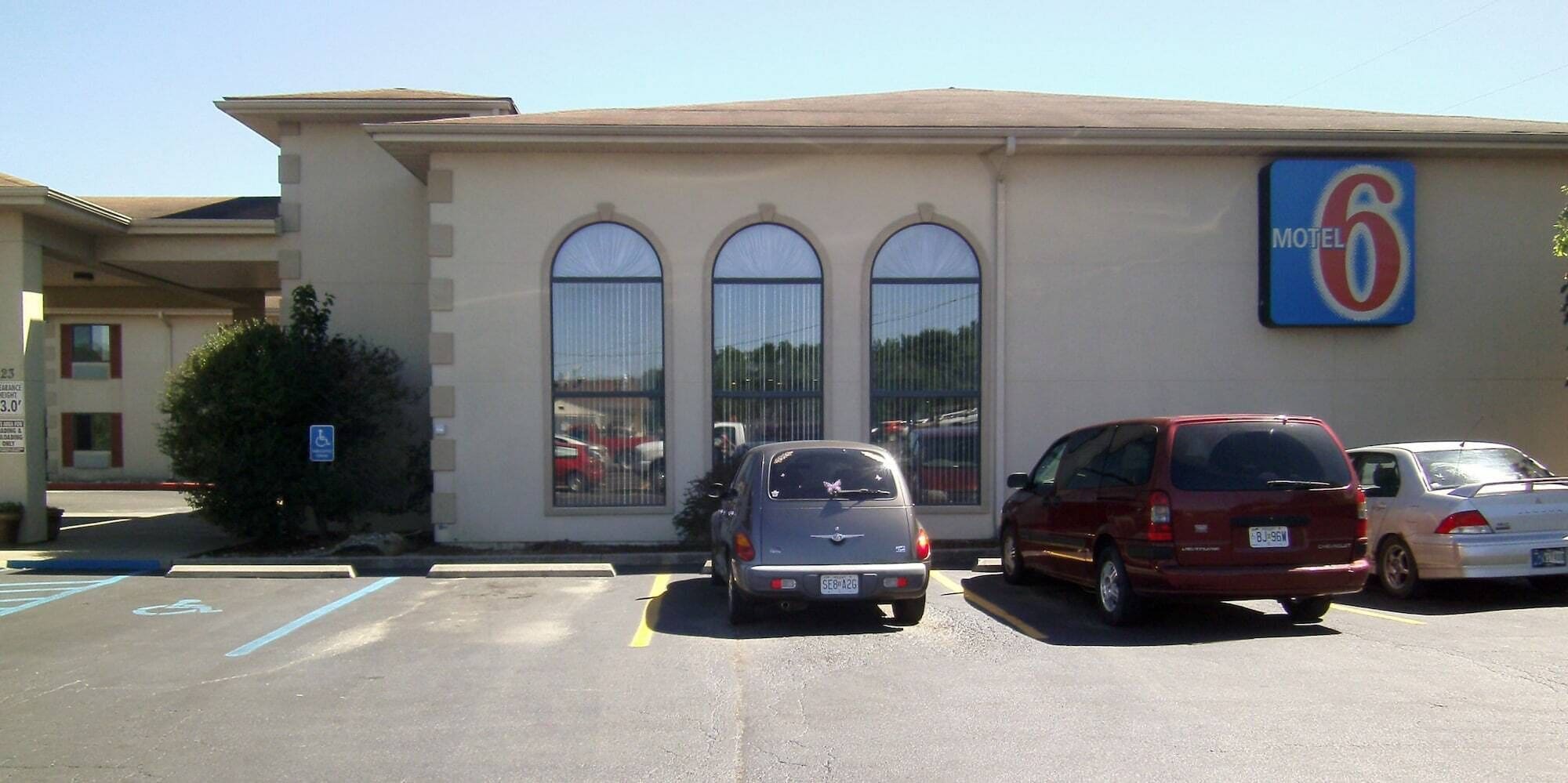 Un motel con tres coches estacionados frente a él, un letrero de estacionamiento para discapacitados y un cielo azul despejado.