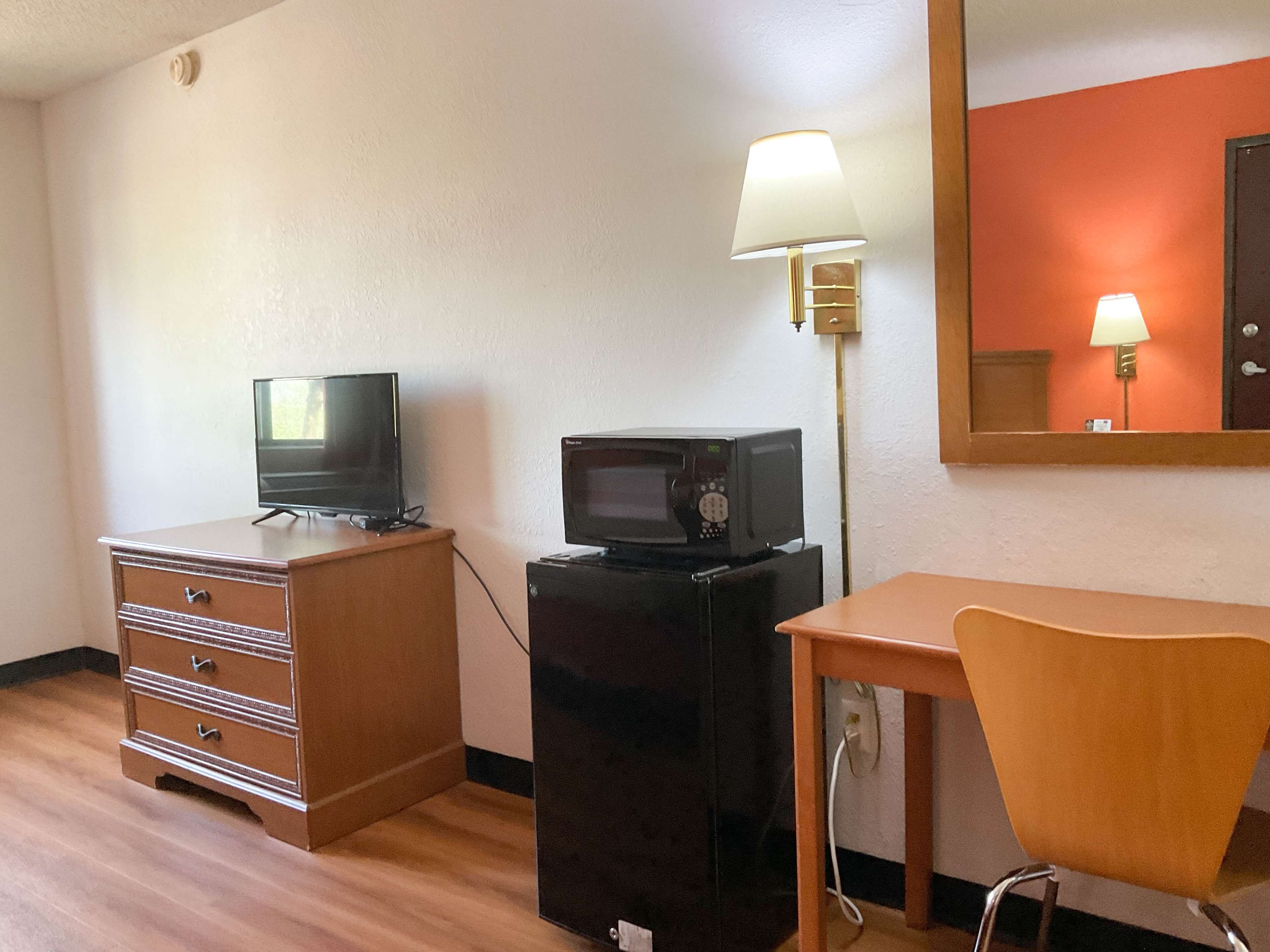 A compact hotel room with a wooden dresser, a television, a microwave, a desk, and a chair.